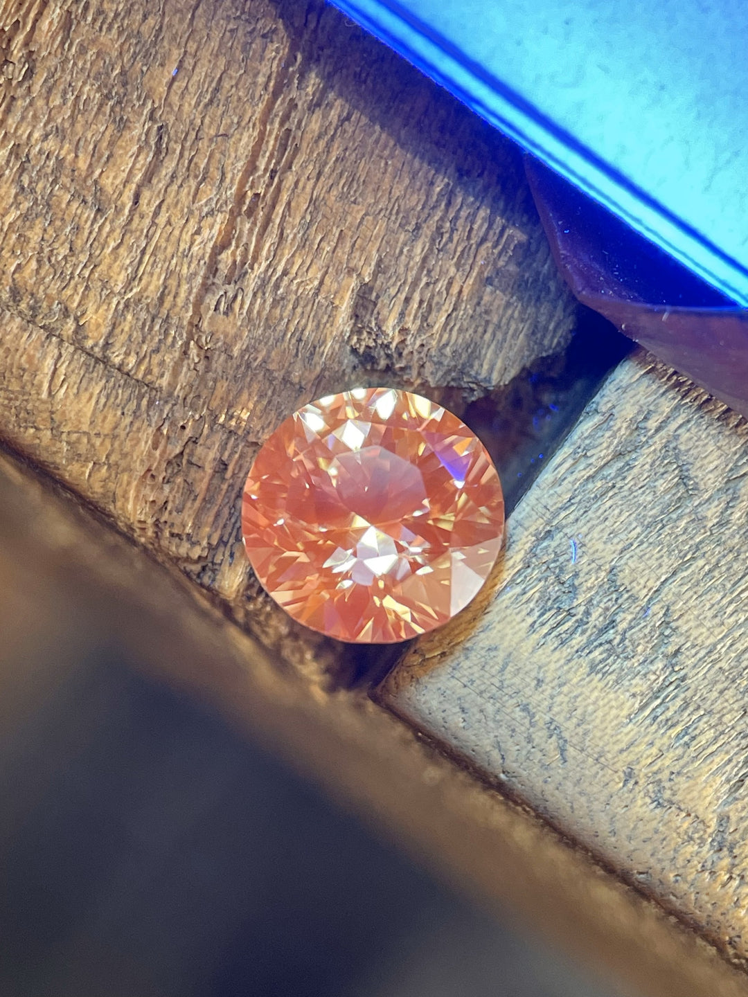 A vibrant 2.57-carat peach sapphire glowing with rich color under warm light, accentuating its brilliance and precision round cut.