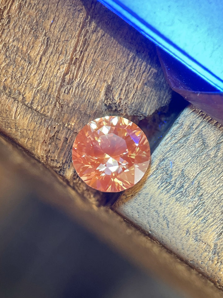 A vibrant 2.57-carat peach sapphire glowing with rich color under warm light, accentuating its brilliance and precision round cut.