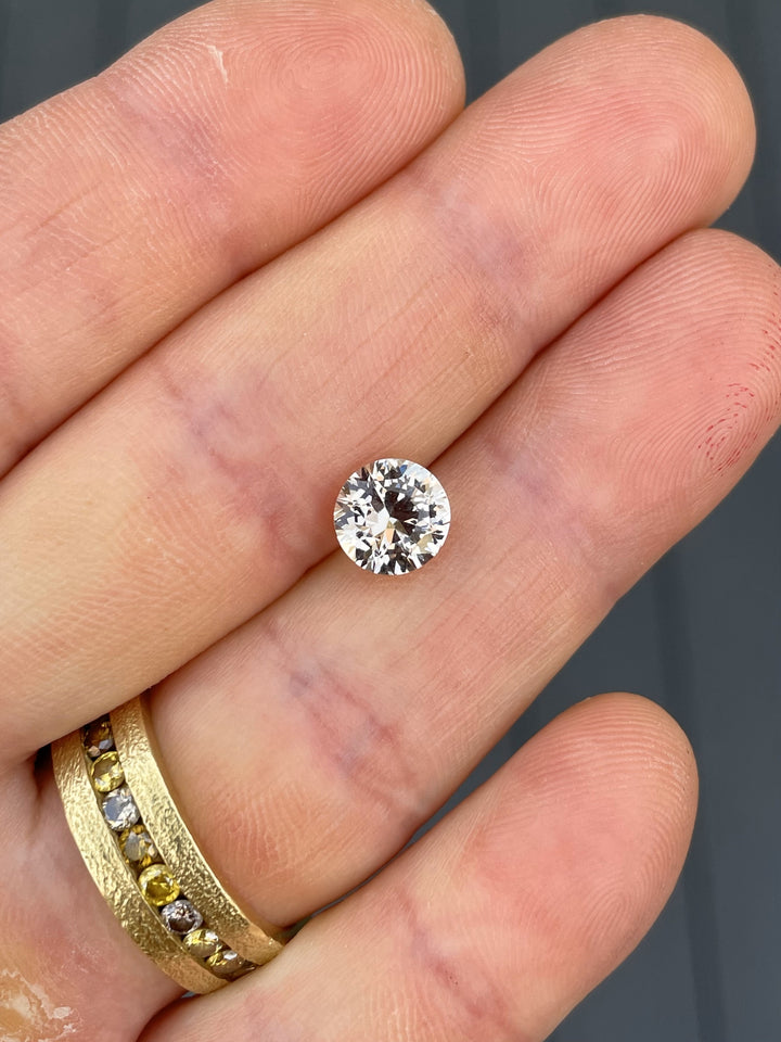 A 2.57-carat round brilliant cut peach sapphire with warm pastel tones, displayed on a hand to highlight its brilliance and size.
