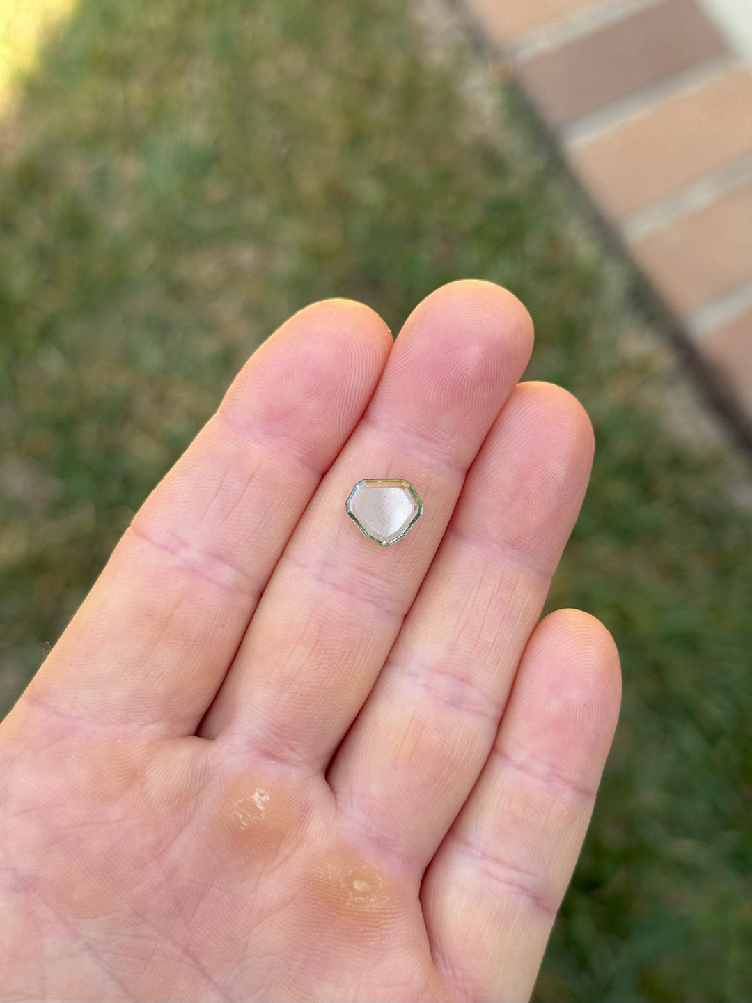 2.58-carat unheated bluish seafoam green Montana sapphire in custom shield portrait cut, held in hand outdoors