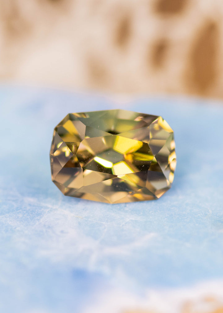 2.59 carat green yellow Tanzanite custom geometric cushion cut placed on display surface, untreated gemstone from Merelani Hills Tanzania highlighting natural color variation and precision cut facets