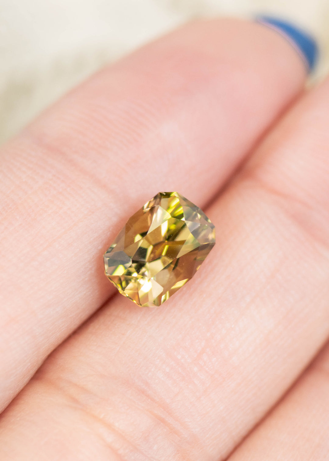 2.59 carat green yellow Tanzanite custom geometric cushion cut gemstone resting on finger, untreated Merelani Hills Tanzania gemstone showing brilliance, precision faceting and natural color for custom jewelry