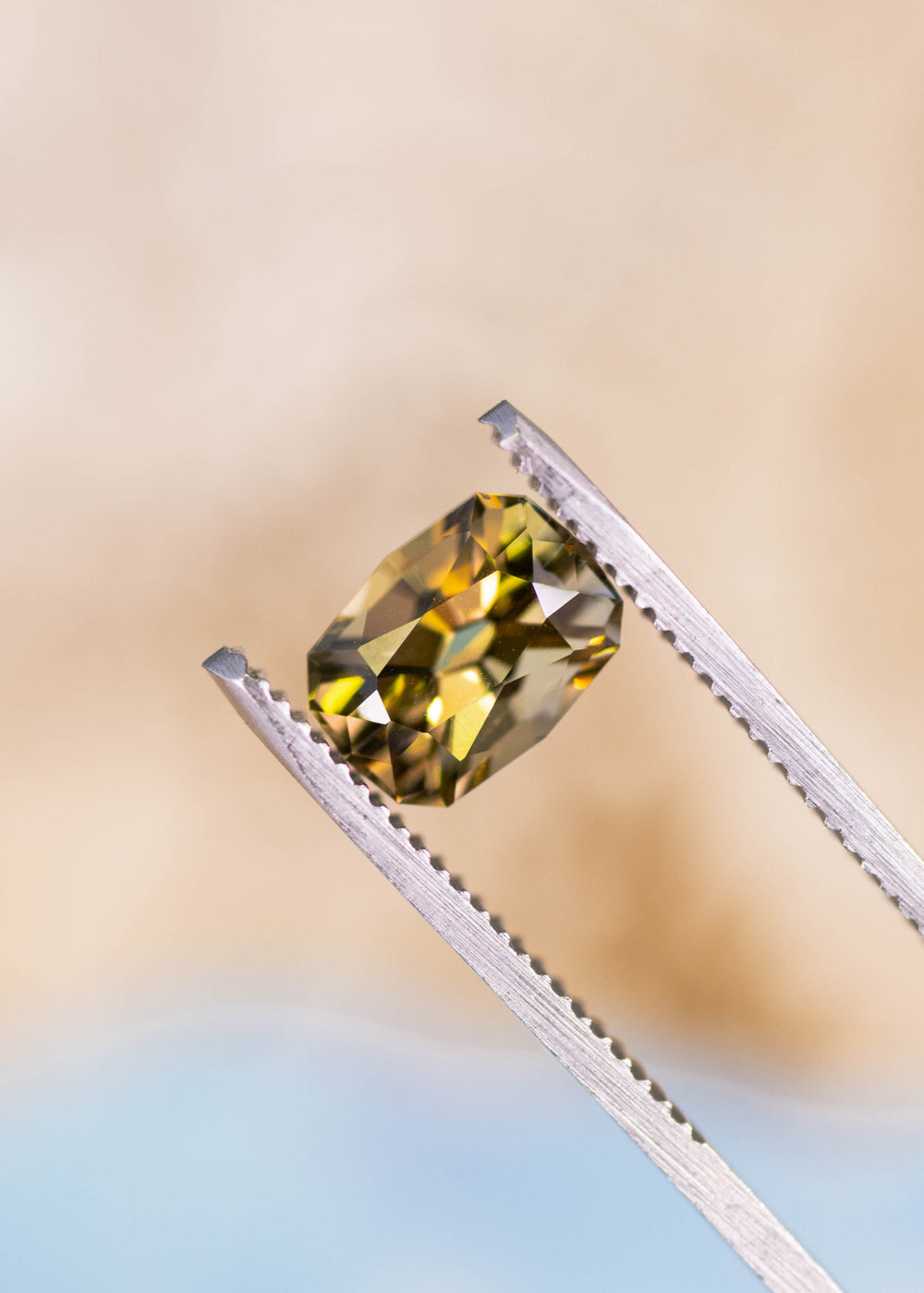 2.59 carat green yellow Tanzanite geometric cushion cut gemstone held in tweezers, untreated Tanzanite from Merelani Hills Arusha Tanzania displaying clarity, sparkle and sharp designer faceting for fine jewelry