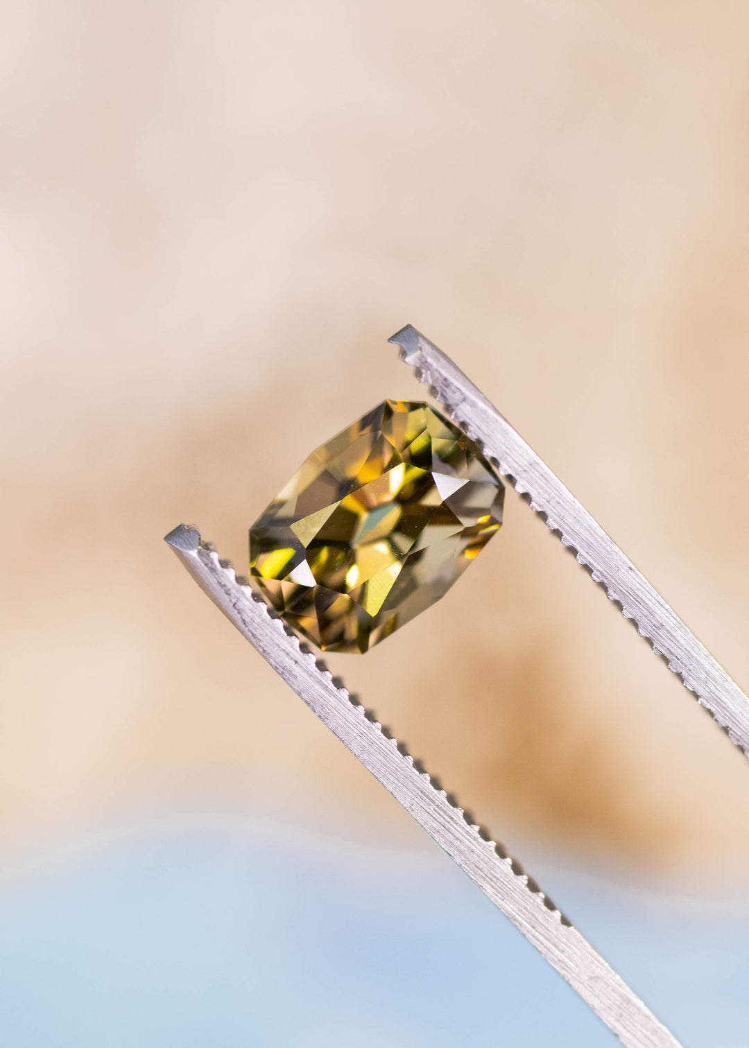 2.59 carat green yellow Tanzanite geometric cushion cut gemstone held in tweezers, untreated Tanzanite from Merelani Hills Arusha Tanzania displaying clarity, sparkle and sharp designer faceting for fine jewelry