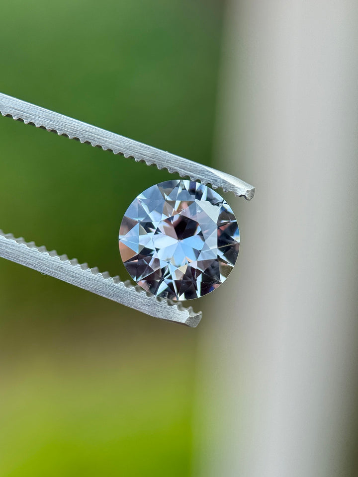 2.60-carat grey to steely violet color-changing sapphire held in tweezers outdoors, showing antique transitional round faceting and high brilliance.