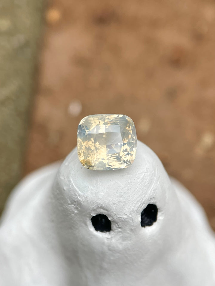 Close-up of a 2.60-carat cushion-cut sapphire with an opalescent pale yellow hue, elegantly displayed on a small sculpture, highlighting its intricate cut and luminous quality.