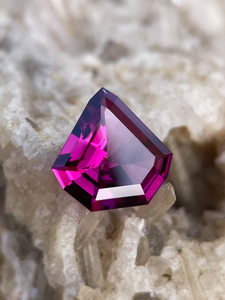 Close-up of a 2.61 carat shield step cut garnet featuring purple, pink, and red hues, sourced from Mombo, Tanzania, and naturally untreated.