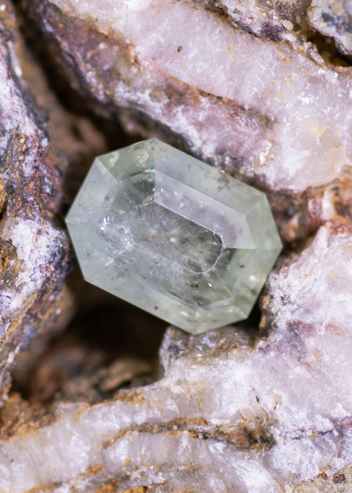 Seafoam green geometric portrait cut Montana sapphire resting between textured quartz rock, showing soft mint tones, visible internal inclusions, and crisp angular facet edges.