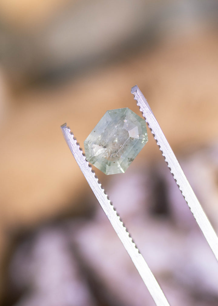 2.62ct seafoam green Montana sapphire held in silver gem tweezers, displaying thick tablet-style depth, geometric facets, and natural inclusions visible through the center.