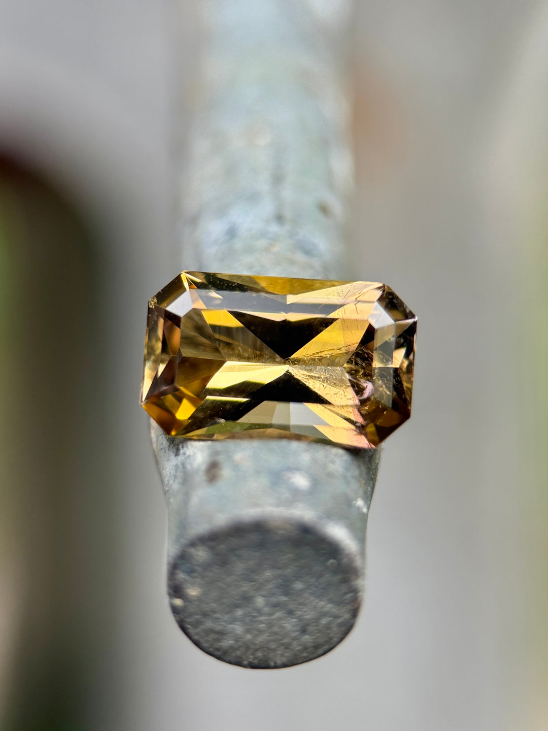 2.63 carat Tanzanite gemstone resting on a metal post, showing radiant flashes of golden yellow, purple, and pink tones in a custom octagon radiant cut, untreated gem from Merelani Hills, Arusha Region, Tanzania.