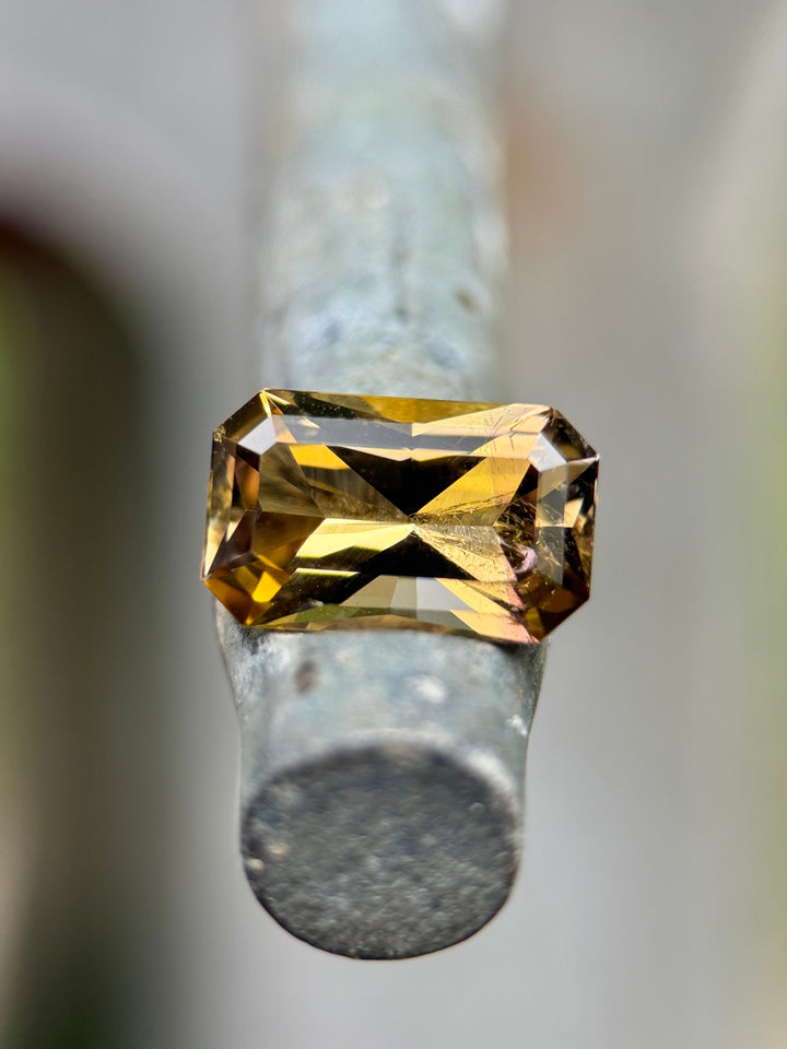 2.63 carat Tanzanite gemstone resting on a metal post, showing radiant flashes of golden yellow, purple, and pink tones in a custom octagon radiant cut, untreated gem from Merelani Hills, Arusha Region, Tanzania.