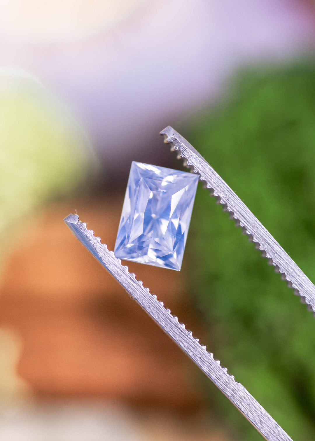 Loose opalescent white to colorless sapphire from Ratnapura, Sri Lanka held in jeweler’s tweezers, displaying the elongated princess cut and crisp facet reflections.