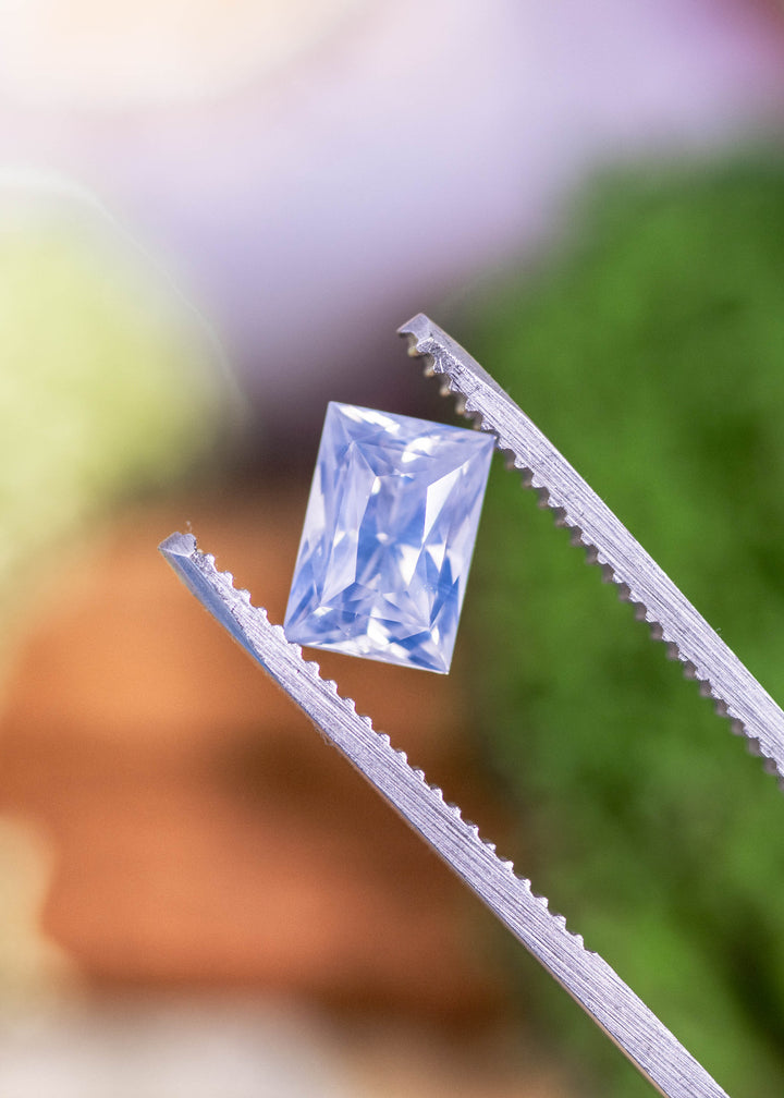 Loose opalescent white to colorless sapphire from Ratnapura, Sri Lanka held in jeweler’s tweezers, displaying the elongated princess cut and crisp facet reflections.