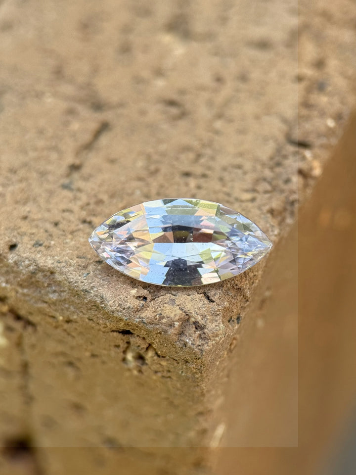 2.68 carat light silvery lilac sapphire placed on textured stone surface, showing precision marquise mixed cut and natural brilliance under sunlight, untreated gem from Sakaraha, Madagascar.