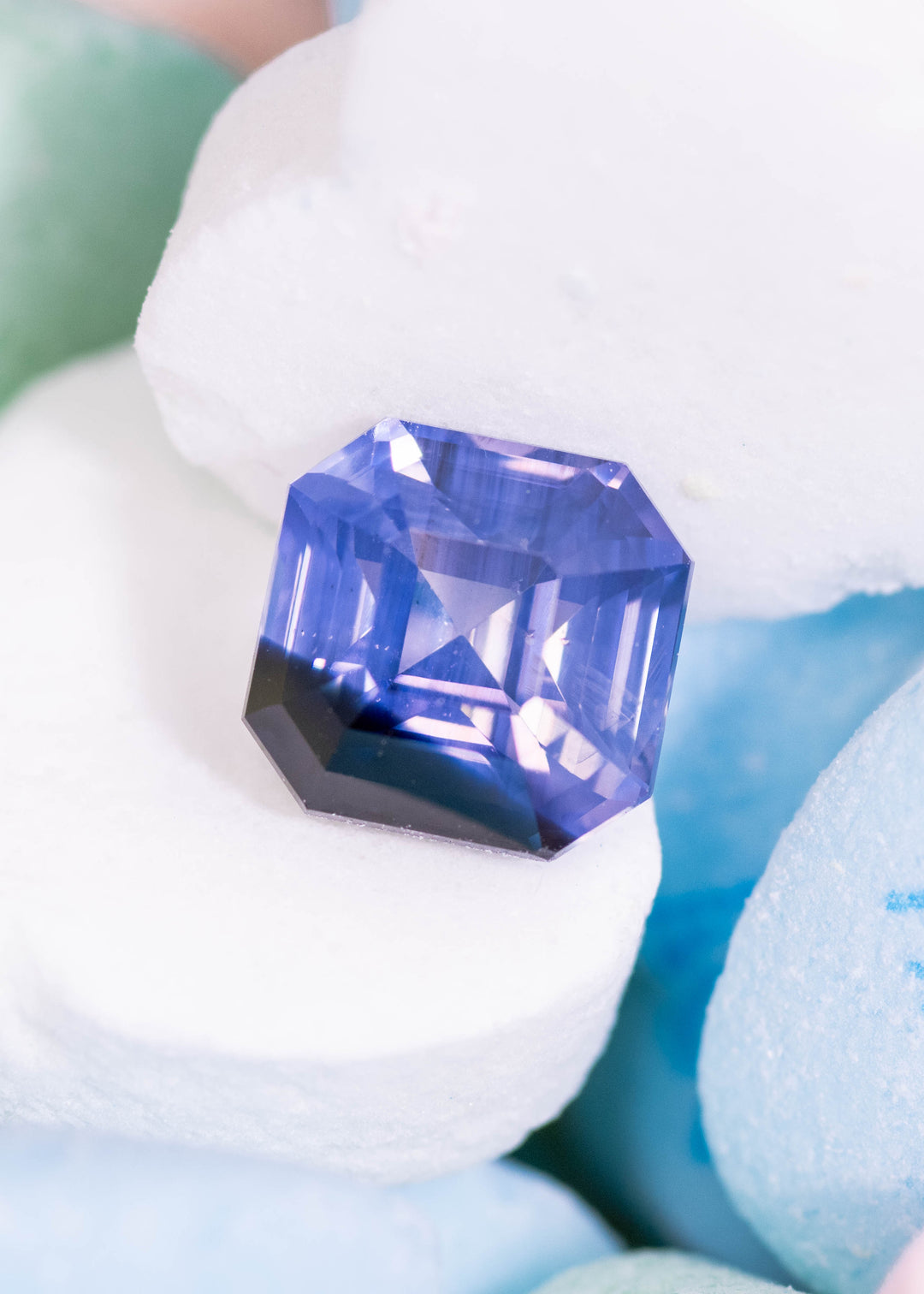 Loose opalescent lavender and periwinkle blue sapphire from Sri Lanka resting on pastel stones displaying the precision Asscher cut and soft color shift.