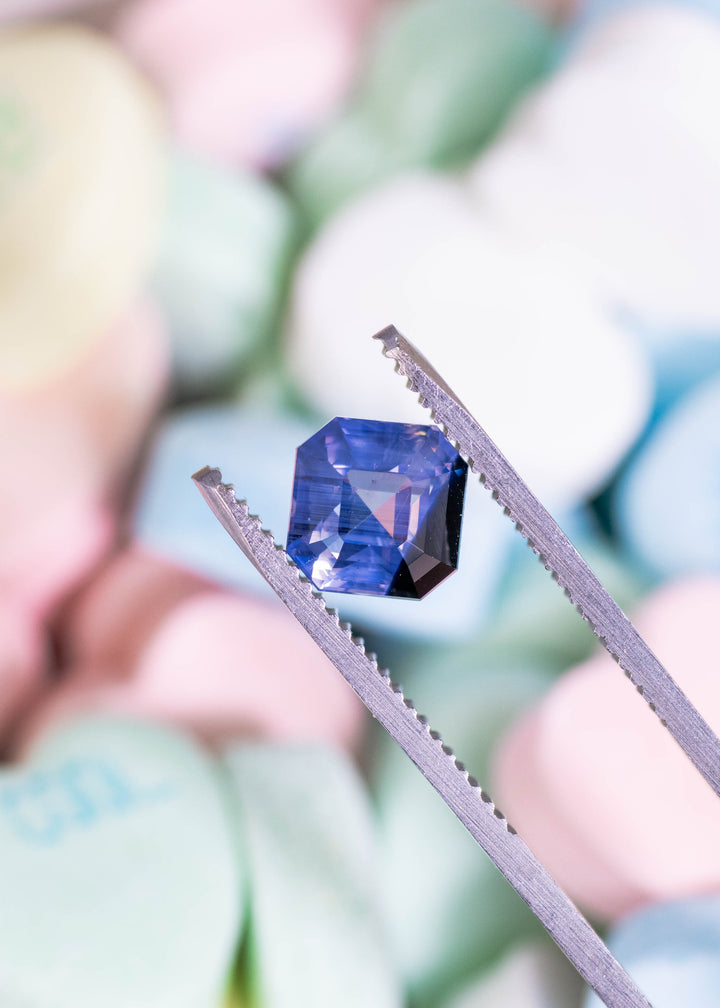 Loose lavender periwinkle blue sapphire from Ratnapura Sri Lanka held in tweezers highlighting the precision Asscher cut and geometric step facets.