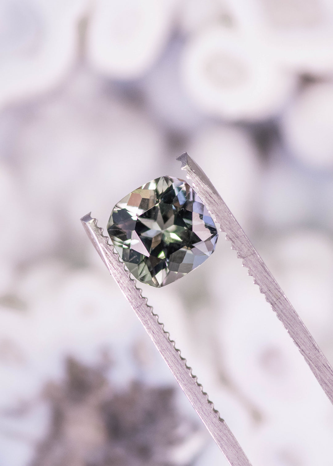 2.74 carat purple green teal Tanzanite square radiant gemstone held in tweezers, custom geometric faceted Tanzanite from Merelani Hills Arusha Tanzania displaying clarity, sparkle and designer cut for fine jewelry