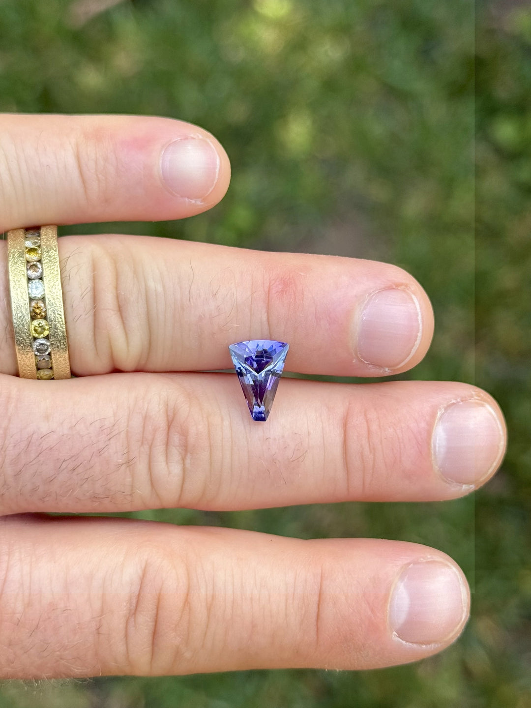 2.74ct Tanzanite gemstone in a custom tapered fan cut displayed on fingers, showcasing vivid teal and purple mermaid tones