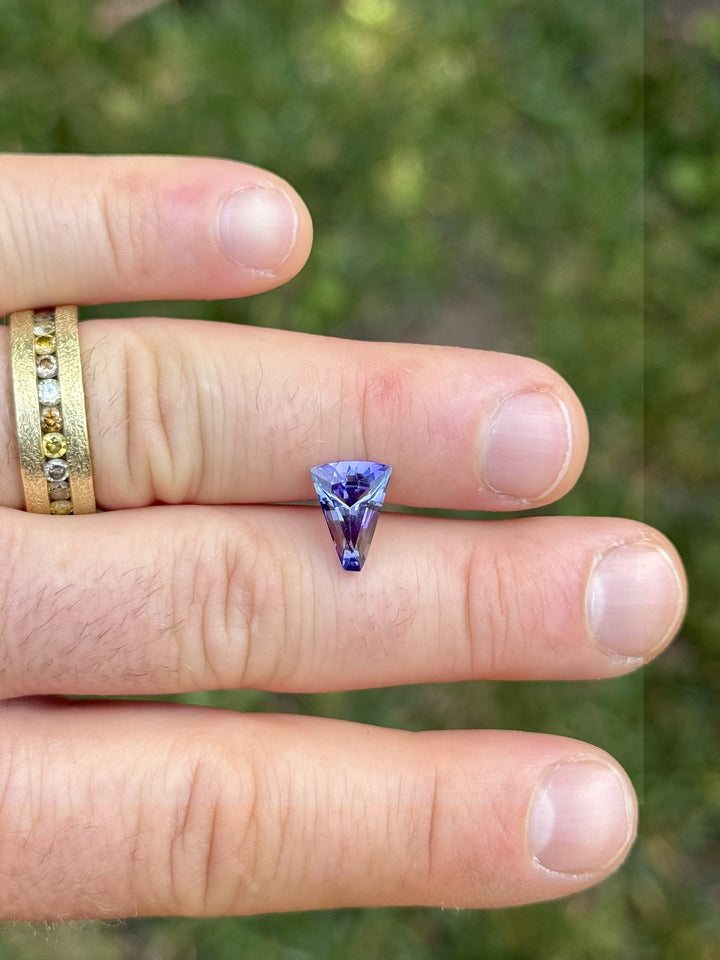 2.74ct Tanzanite gemstone in a custom tapered fan cut displayed on fingers, showcasing vivid teal and purple mermaid tones