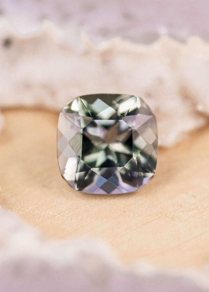 2.74 carat purple teal green Tanzanite custom geometric square radiant cut placed on display surface, Merelani Hills Tanzania origin gemstone highlighting sharp facet pattern and natural trichroic color