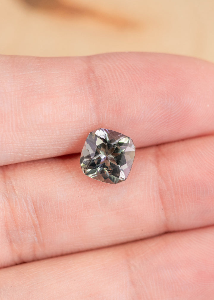 2.74 carat purple teal green Tanzanite square radiant gemstone resting on finger, custom geometric cut from Merelani Hills Tanzania showing color shift, brilliance and precision faceting for custom jewelry