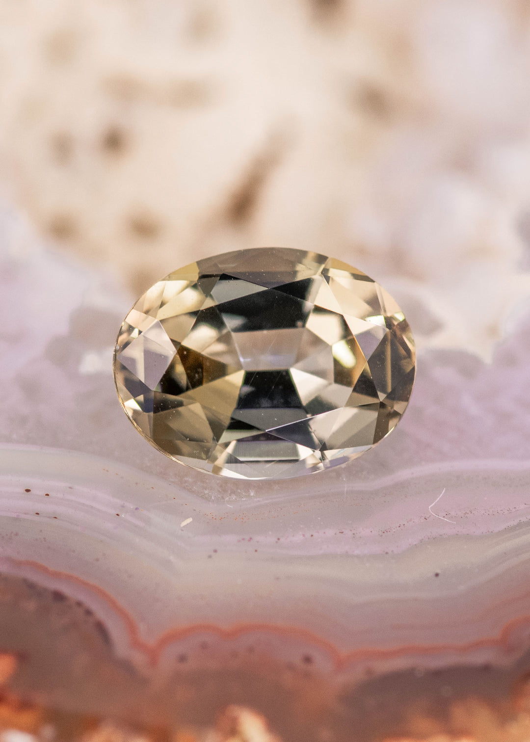 Natural 2.77 carat Tanzanite oval mix cut gemstone on agate surface showing green gold color shift and detailed faceting pattern