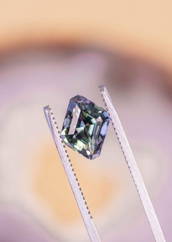 Loose 2.81ct parallelogram Tanzanite held in gem tweezers displaying mermaid violet blue teal green hues and crisp step cut precision