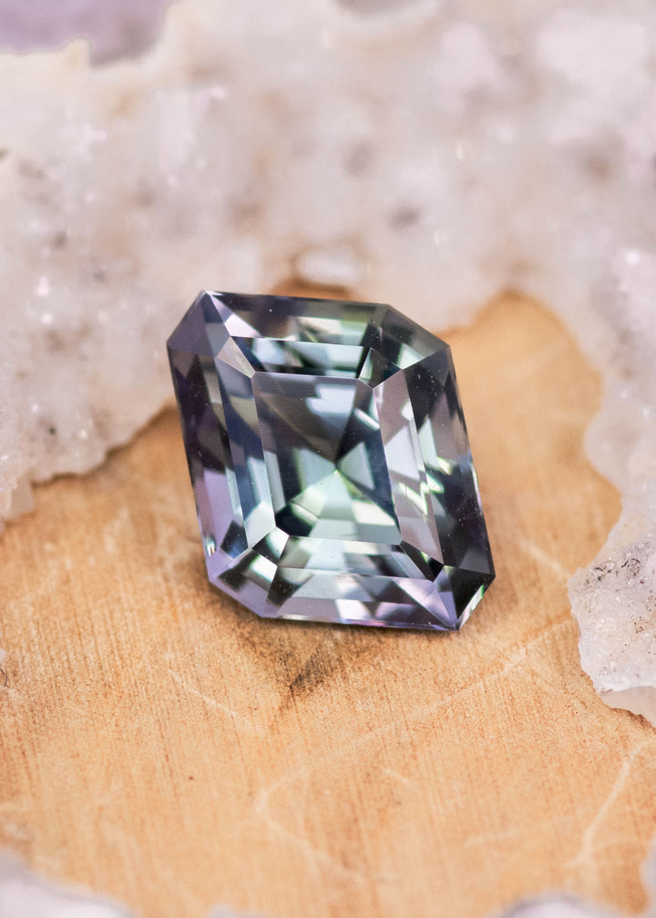 Natural 2.81 carat Tanzanite custom geometric step cut parallelogram on wooden surface showing blue teal green violet brilliance from Tanzania