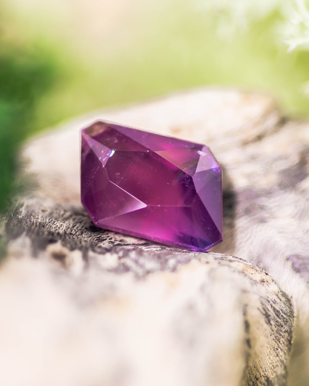 Close-up of 2.85CT pink and purple sapphire placed on natural wood texture, showing deep magenta flashes and clean facet lines of its custom radiant emerald cut, unheated sapphire from Umba River Valley, Tanzania.