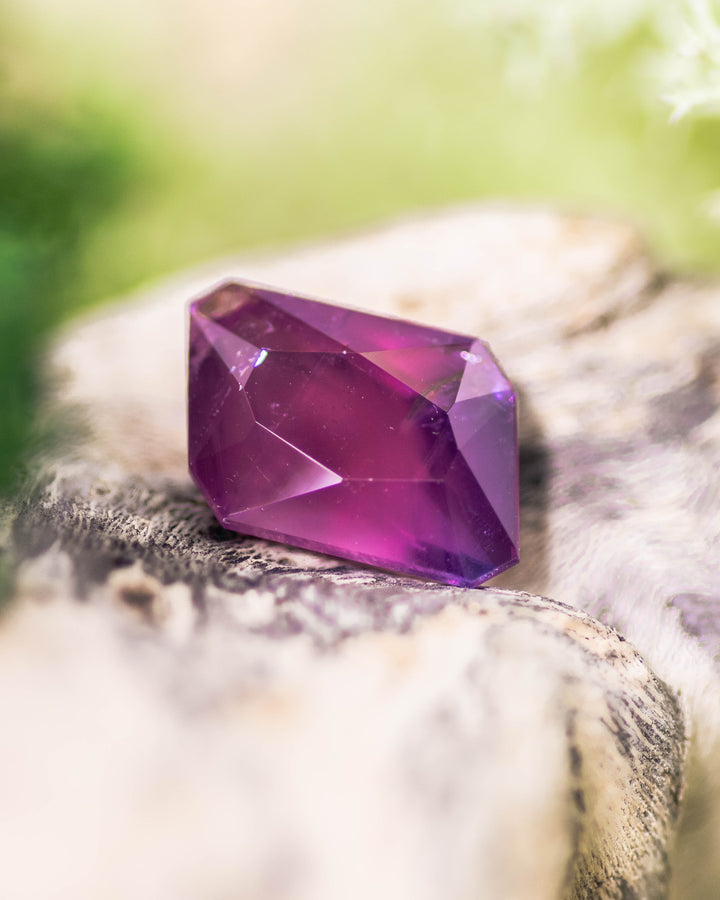 Close-up of 2.85CT pink and purple sapphire placed on natural wood texture, showing deep magenta flashes and clean facet lines of its custom radiant emerald cut, unheated sapphire from Umba River Valley, Tanzania.