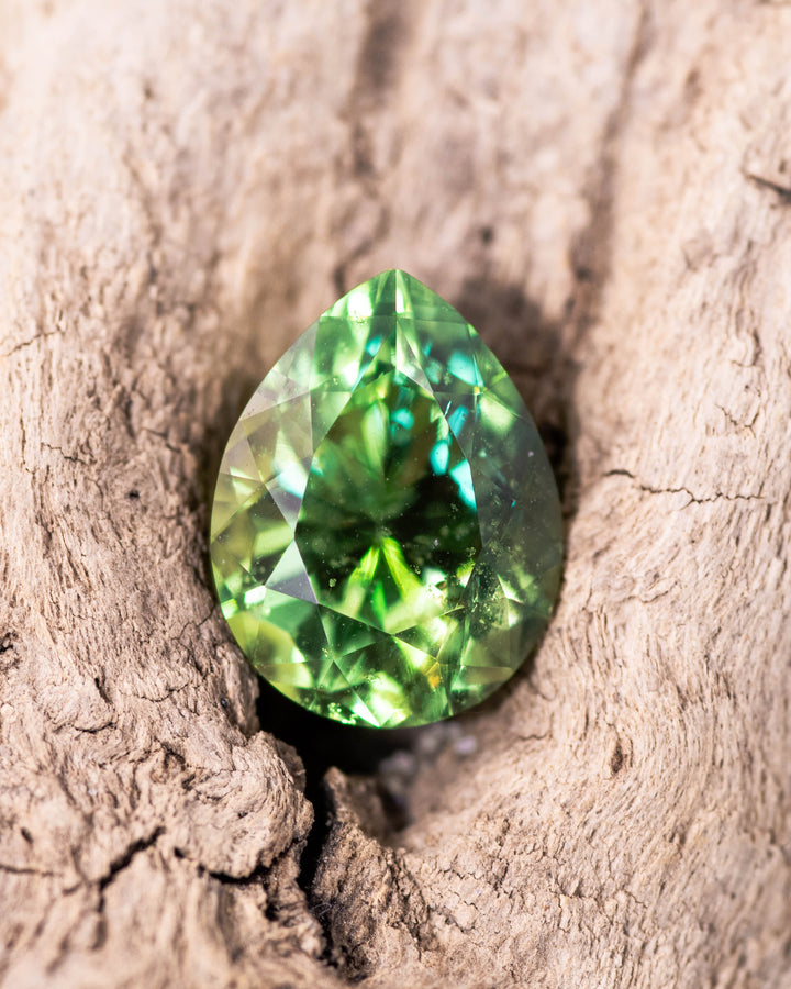 2.85 carat electric lime green Tsavorite garnet resting in a natural wood crevice, showing intense color, fire, and brilliance of the modified brilliant pear cut, untreated Tsavorite from Kenya.