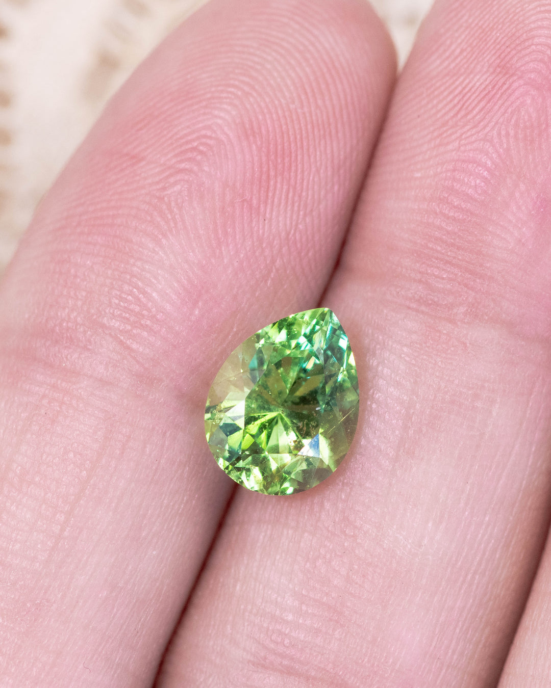 2.85 carat Tsavorite garnet placed on fingertips, reflecting vivid electric lime green hues and internal brilliance through the modified brilliant pear cut, untreated gemstone from Kenya.