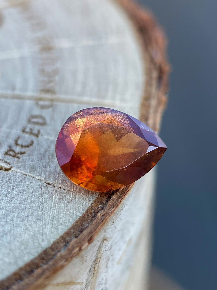 Natural 2.90 carat orange sapphire in a modified pear cut from Umba River, Tanzania, displayed on a rustic wooden background.