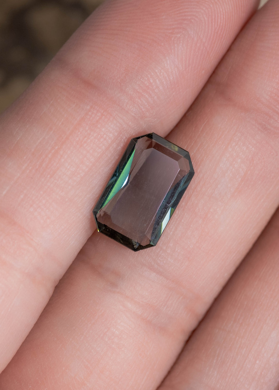 2.96 carat teal blue-green purple Tanzanite resting on finger, low profile custom emerald cut gemstone from Tanzania highlighting elongated rectangular symmetry, refined step faceting and sleek contemporary custom jewelry appeal