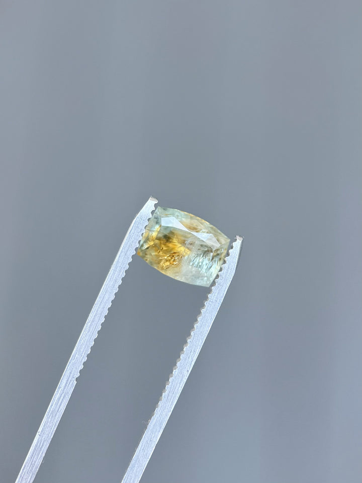 Macro shot of a 2.99ct unheated Montana sapphire held in tweezers, showing orange and teal parti color in a custom elongated cushion cut.