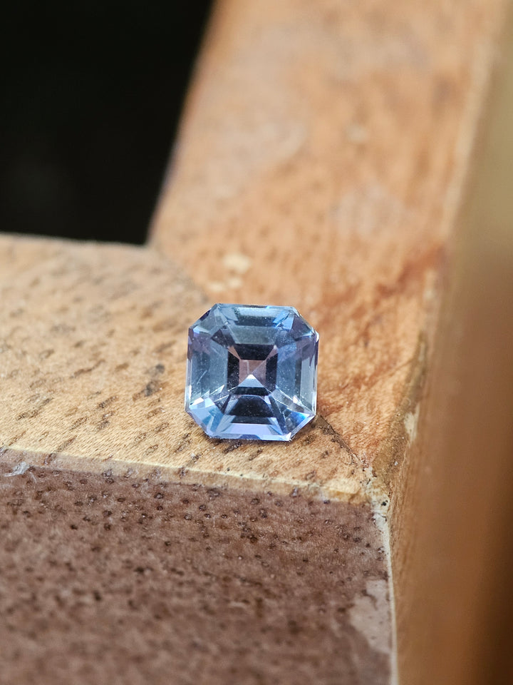 1.10 carat Asscher cut Tanzanite gemstone with teal, blue-green, and purple tones, captured on a wooden surface to highlight its sharp lines and vibrant colors.