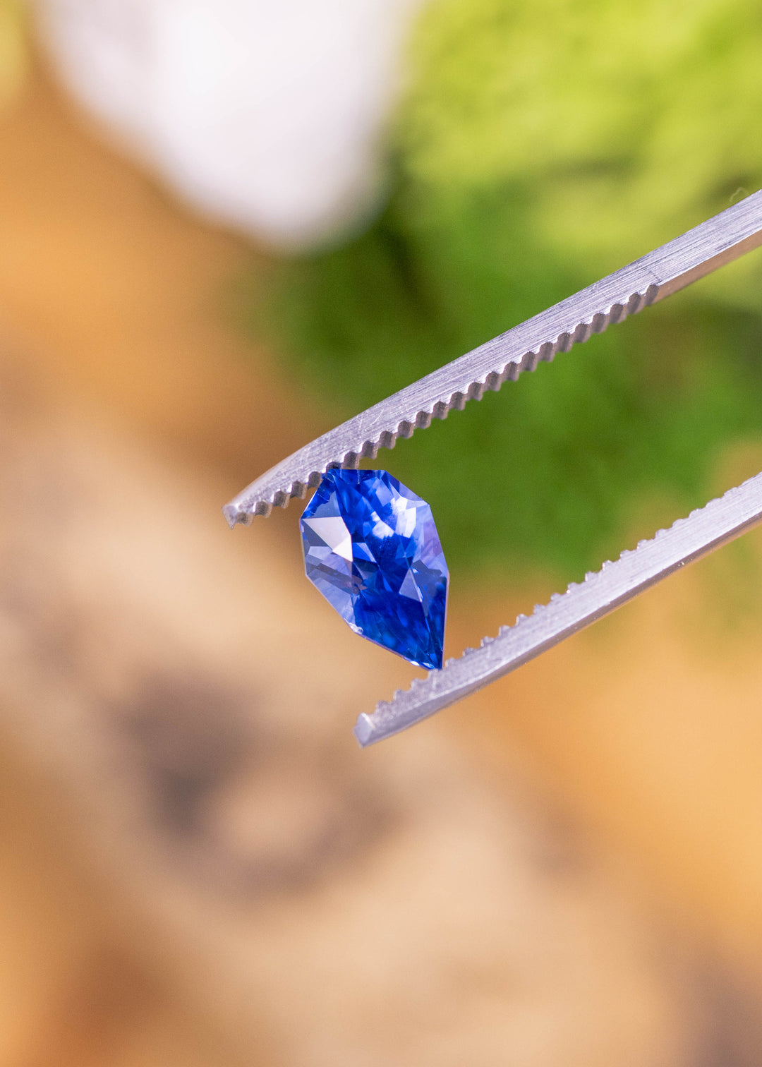 Loose blue purple sapphire from Ratnapura Sri Lanka held in tweezers highlighting the custom geometric pear cut and vivid royal blue color.