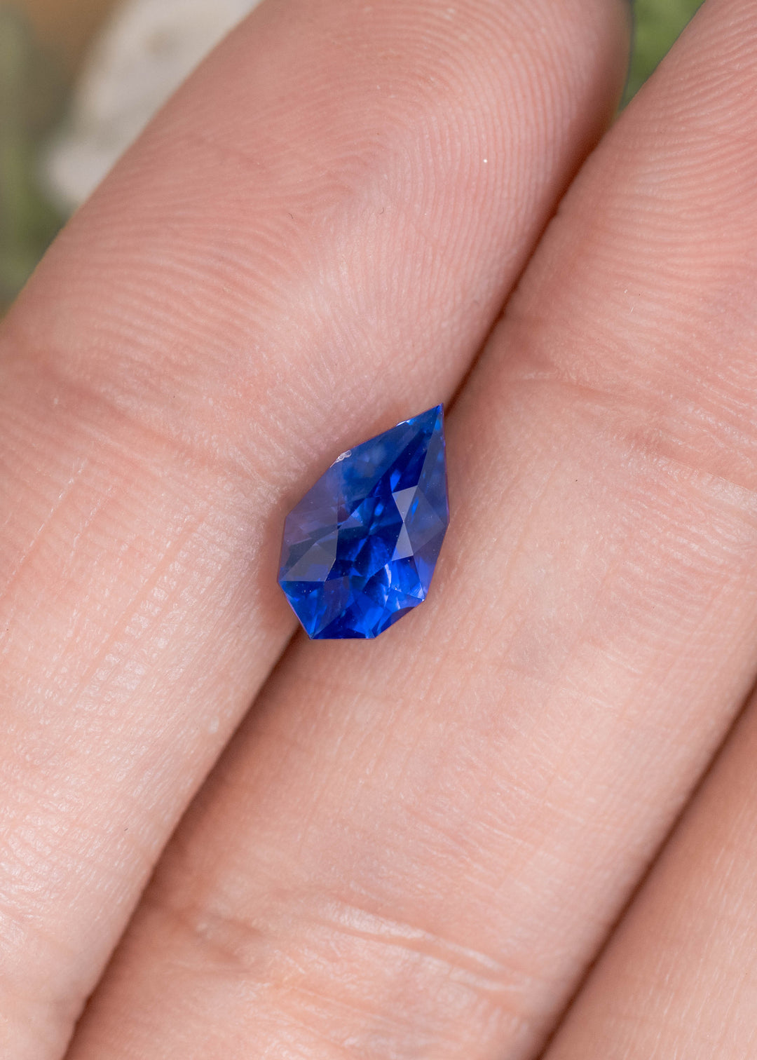 Loose blue and purple sapphire from Sri Lanka resting on fingertips displaying the custom mix pear cut and deep saturated color.