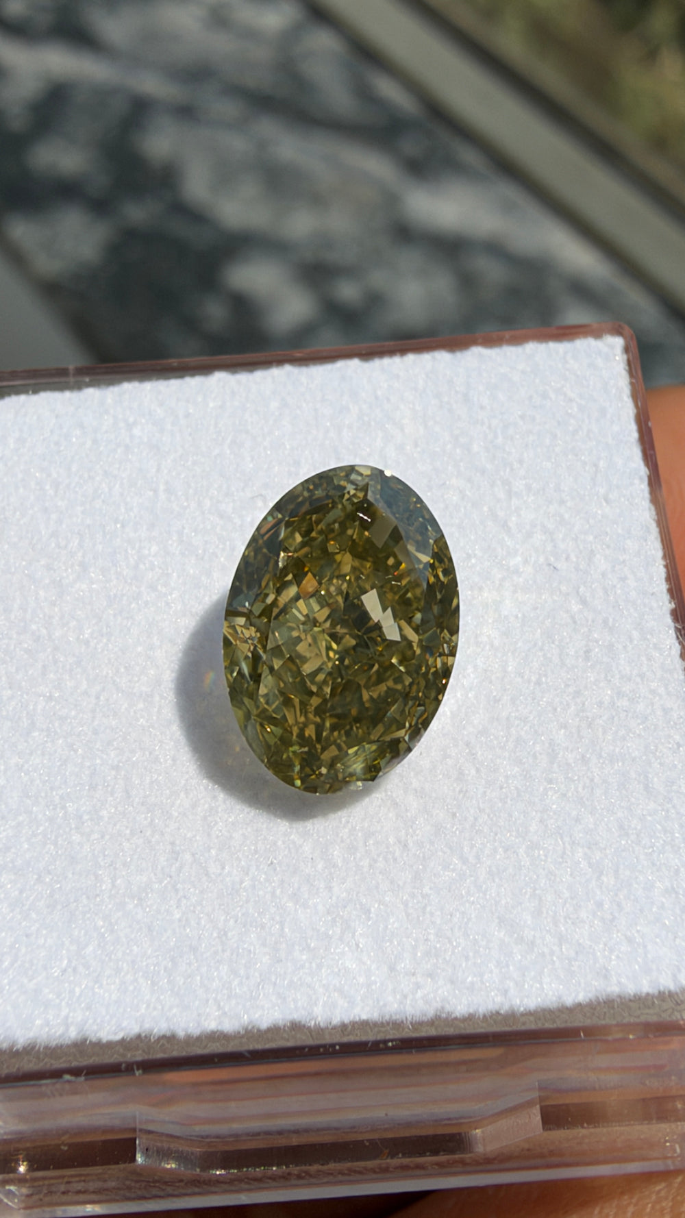 Close-up photograph of a 3.01ct Fancy Brownish Greenish Yellow oval diamond highlighting its faceting and complex fancy color