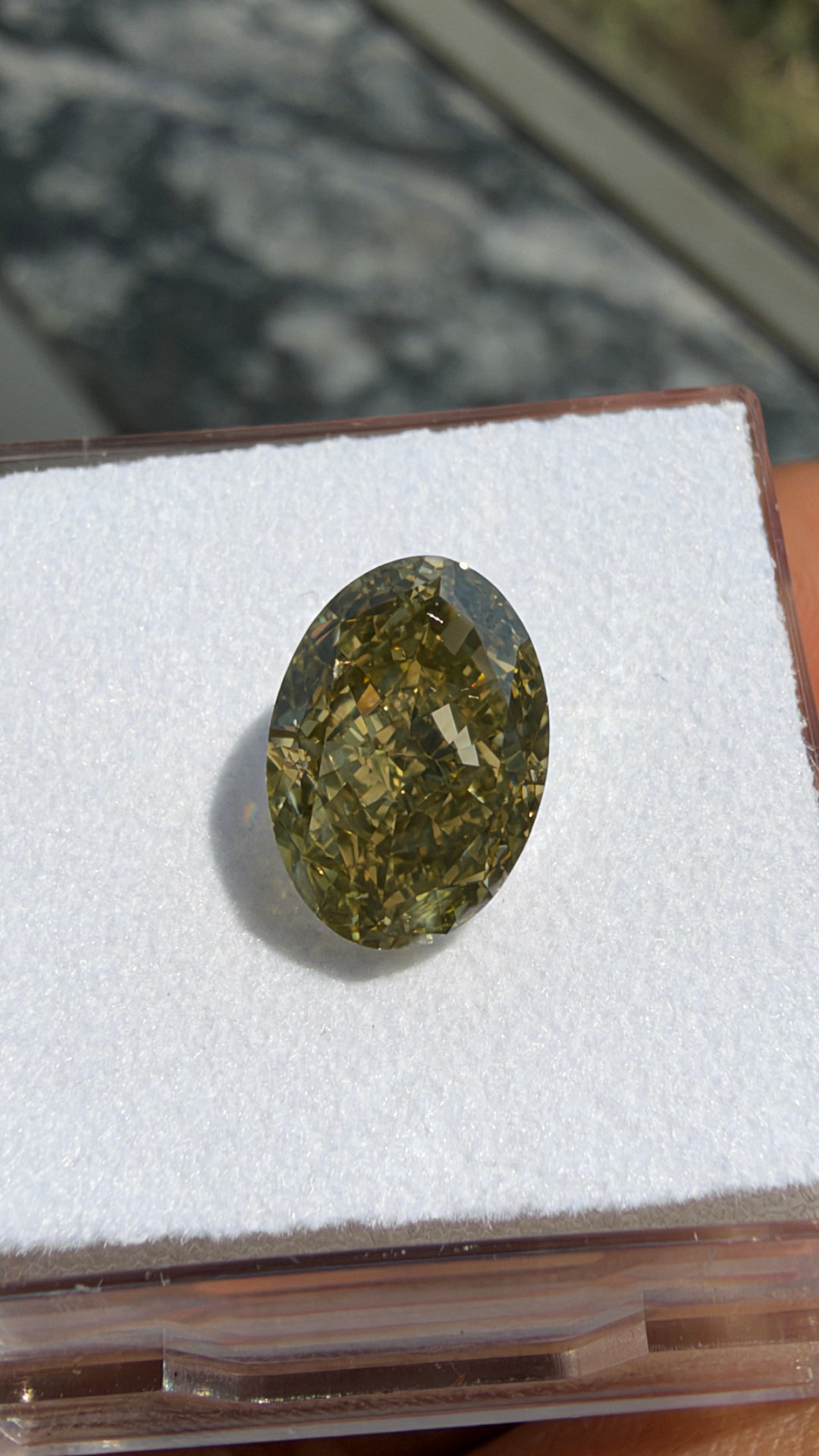 Close-up photograph of a 3.01ct Fancy Brownish Greenish Yellow oval diamond highlighting its faceting and complex fancy color