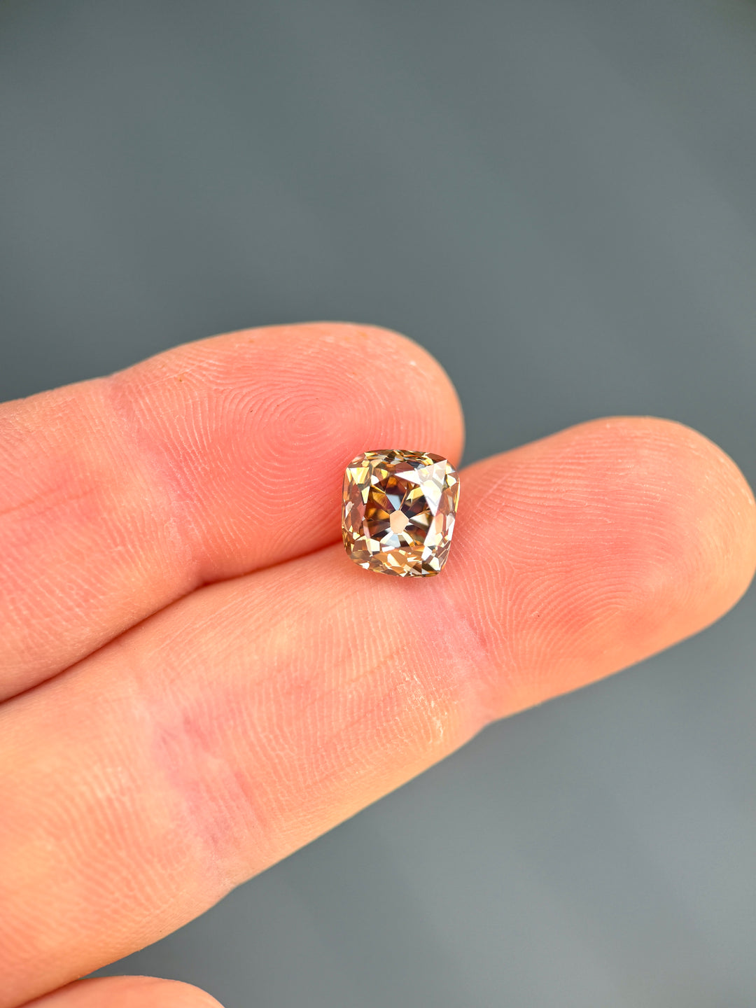 Close-up of a 3.93 carat Canadian champagne diamond on fingertips, highlighting its antique cushion shape, VVS1 clarity, and warm brown-gold brilliance.