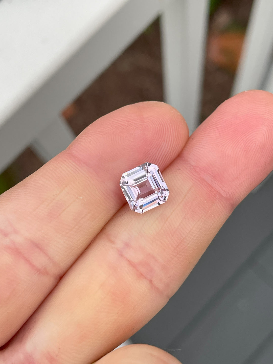 Natural 3.02 carat pink and lavender sapphire in custom square emerald cut resting on fingertip, showcasing its clarity and geometric brilliance under daylight