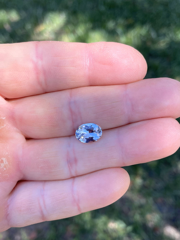 Hand holding a 3.03 carat oval brilliant cut sapphire with lavender, pink, and purple hues from Sakaraha, Madagascar.