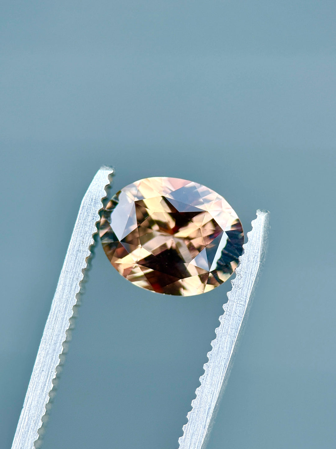 3.04 carat pumpkin spice sapphire oval precision mixed cut from Madagascar held in gem tweezers showing autumn purplish reddish brown color shift