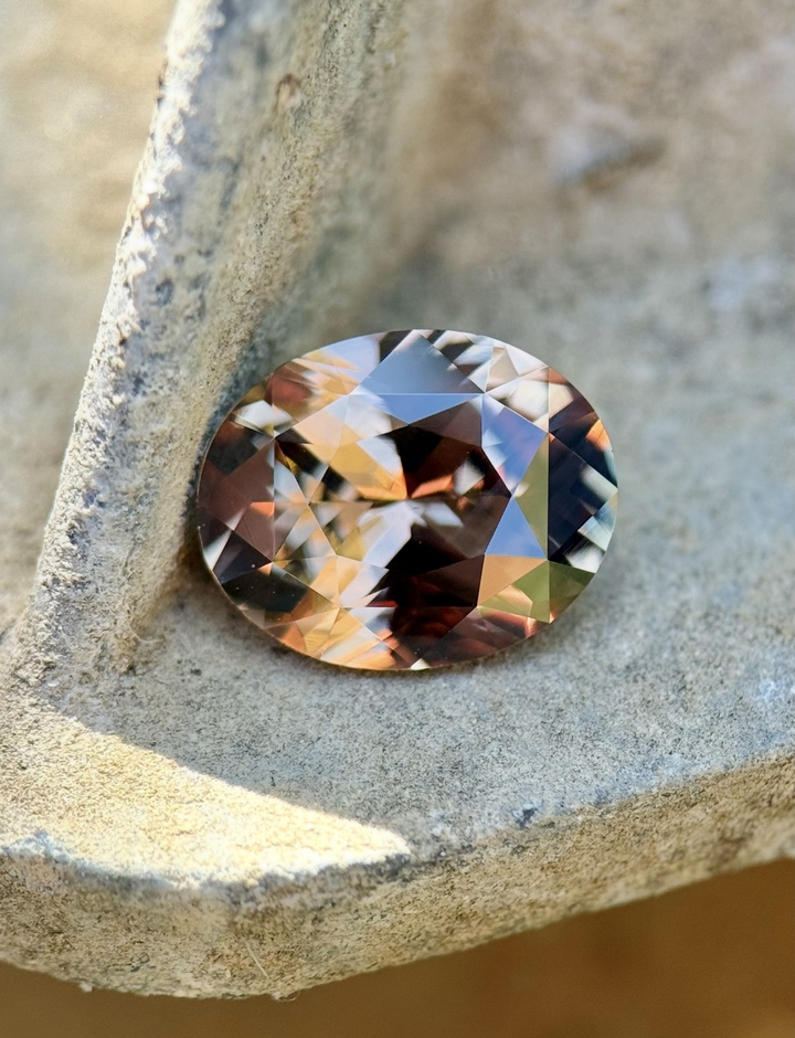 Pumpkin spice autumn color shift sapphire 3.04 carat oval precision cut from Sakaraha Madagascar resting on natural stone macro gemstone photography