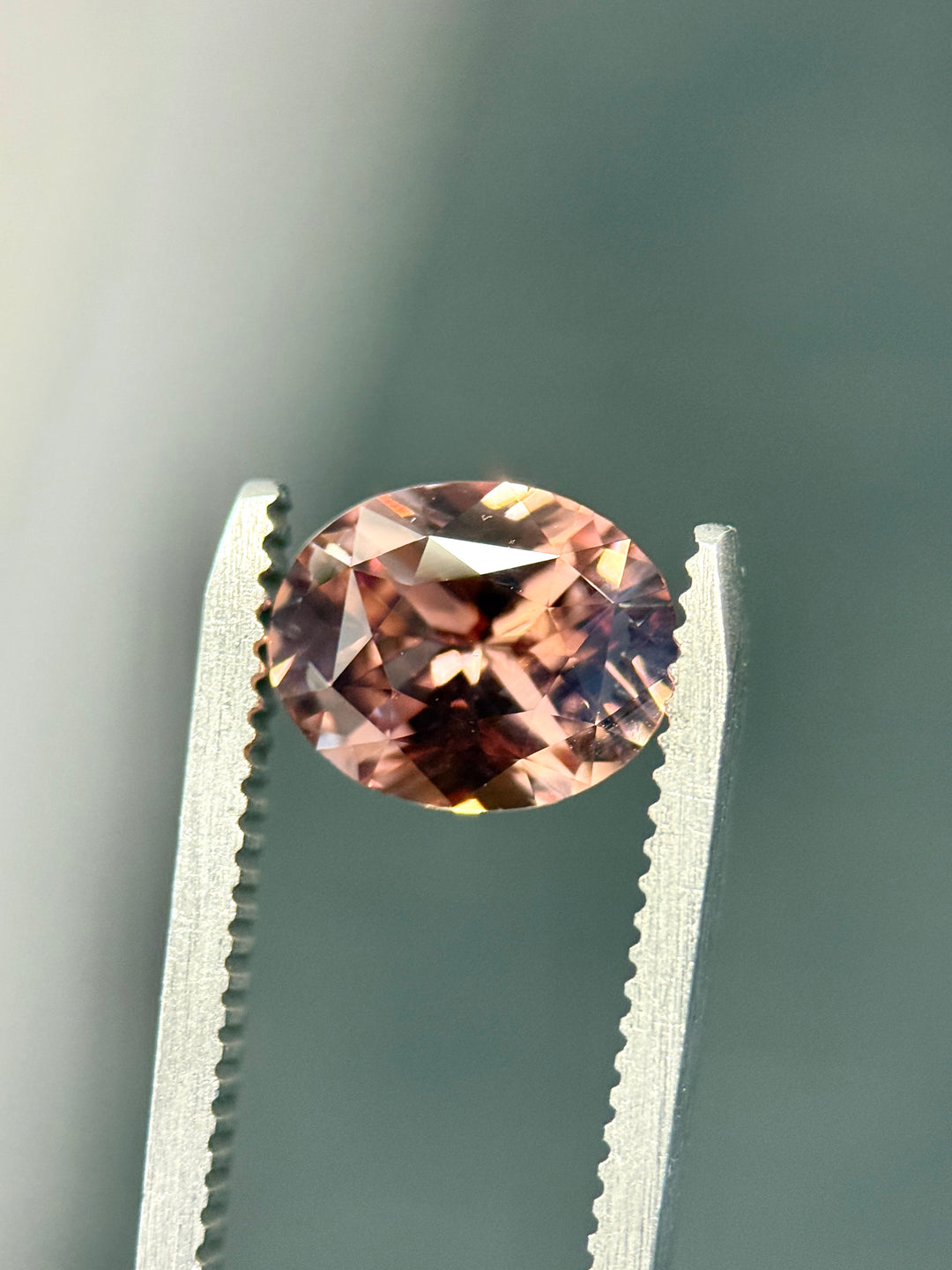 loose Madagascar sapphire pumpkin spice autumn color shift oval mixed cut precision gemstone macro photography in gem tweezers