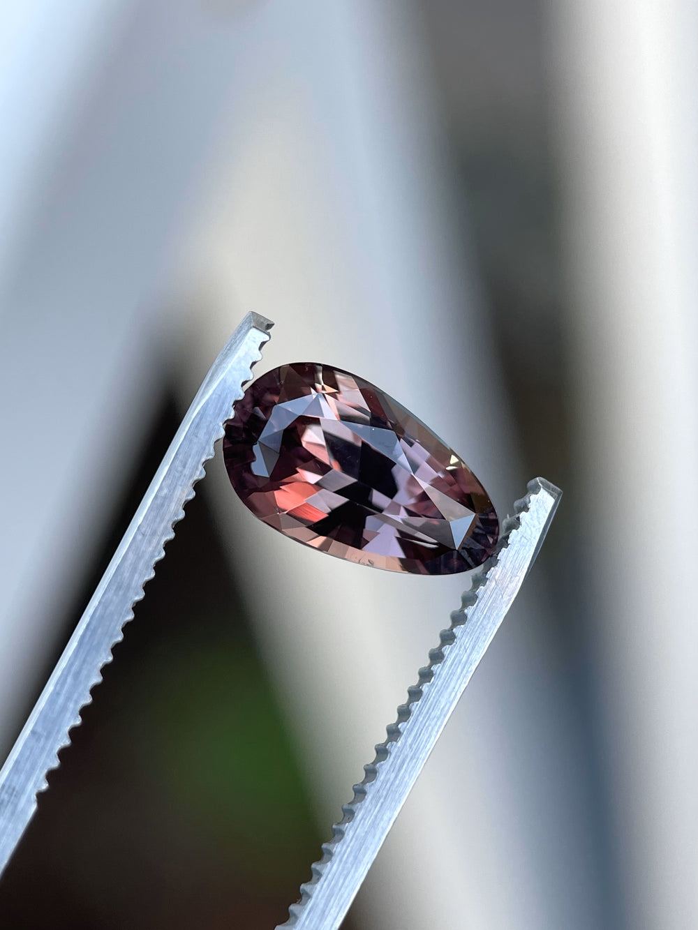 A high-definition image of a pear-shaped 3.09-carat color-change sapphire from Songea, Tanzania, held in tweezers to emphasize its brilliance and heated treatment.