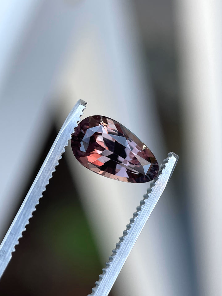 A high-definition image of a pear-shaped 3.09-carat color-change sapphire from Songea, Tanzania, held in tweezers to emphasize its brilliance and heated treatment.