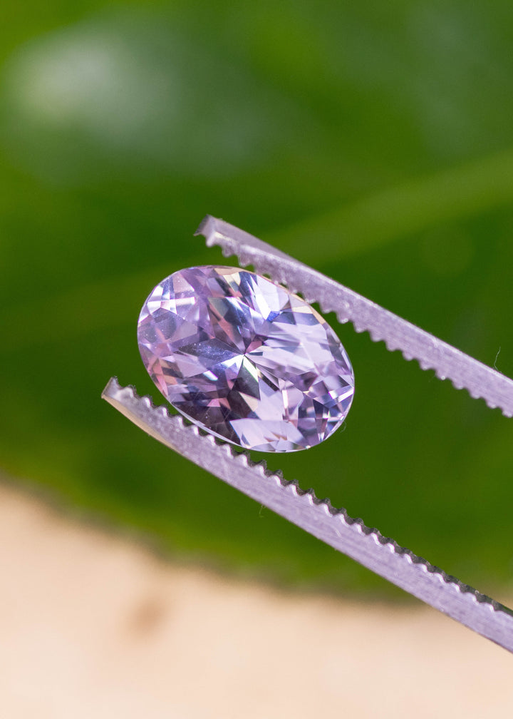 Loose lavender pink purple sapphire from Madagascar resting on a green leaf showing the precision oval mixed cut and soft pastel color in natural light.