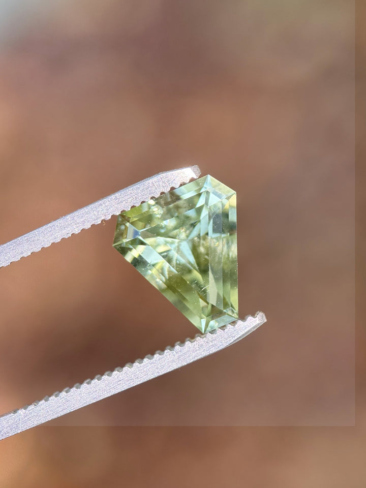 3.26 carat mint green tourmaline held in gemstone tweezers, displaying custom shield step cut facets and vivid pastel green tones, untreated natural gem from Congo, Africa.